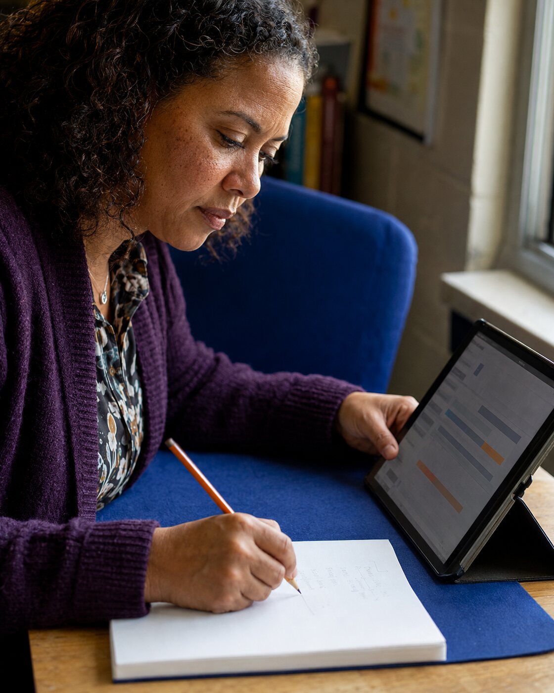 A person takes notes while reviewing an abstract chart on a tablet.