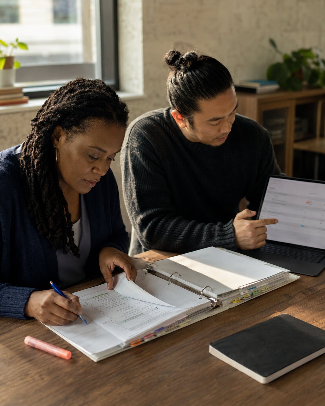 Two colleagues review a tabbed evidence binder and an unbranded digital records workspace together.